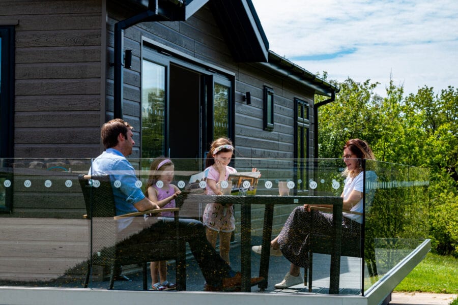 Family looking at a Wenningdale Escapes brochure while sat outside on the veranda on outdoor furniture at Wenningdale Escapes