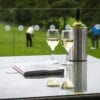Magazines, wine glasses and wine bottle in an ice bucket sitting on an outdoor glass table overlooking a golf course