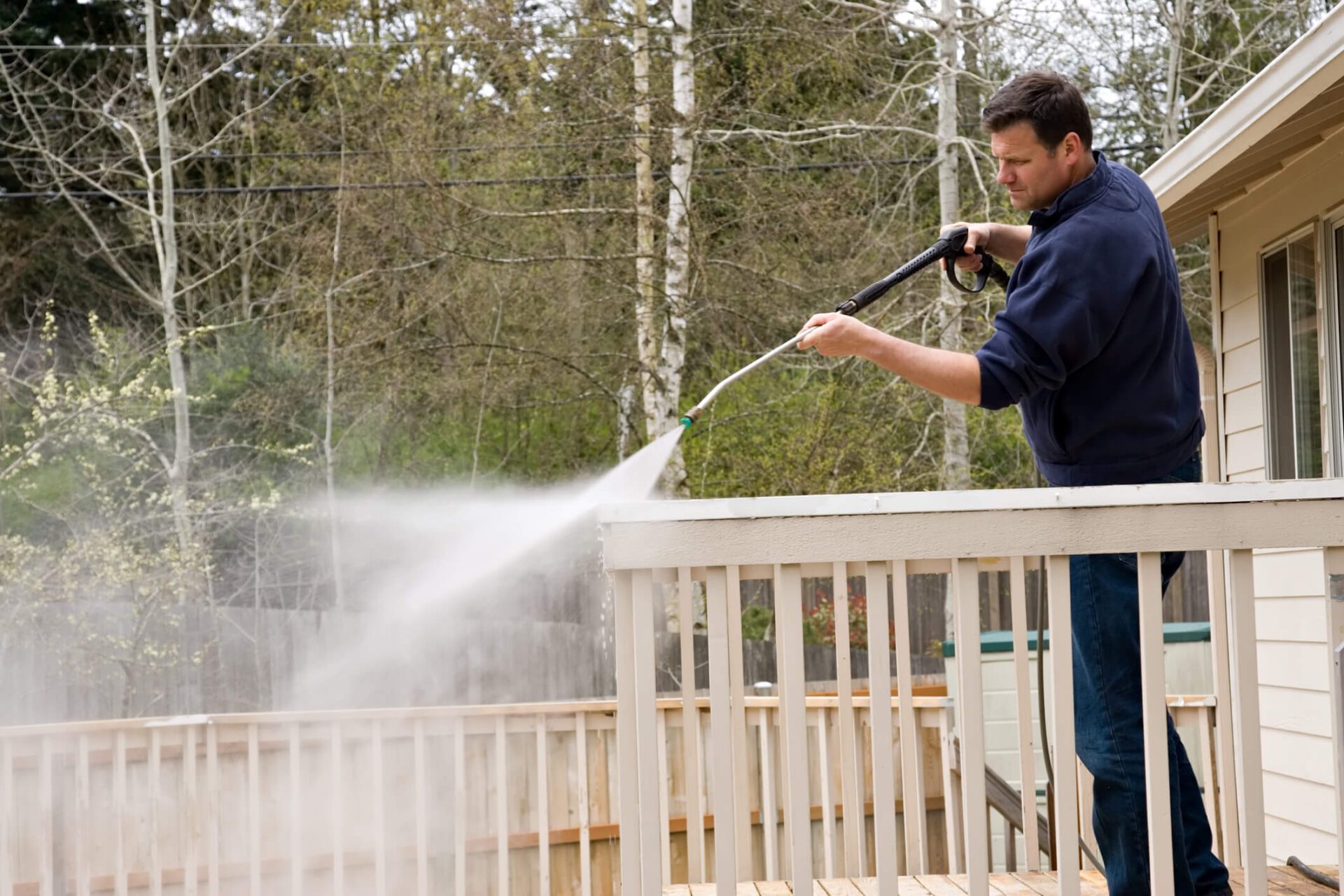 Man cleaning off exterior holiday home deck using a pressure washer